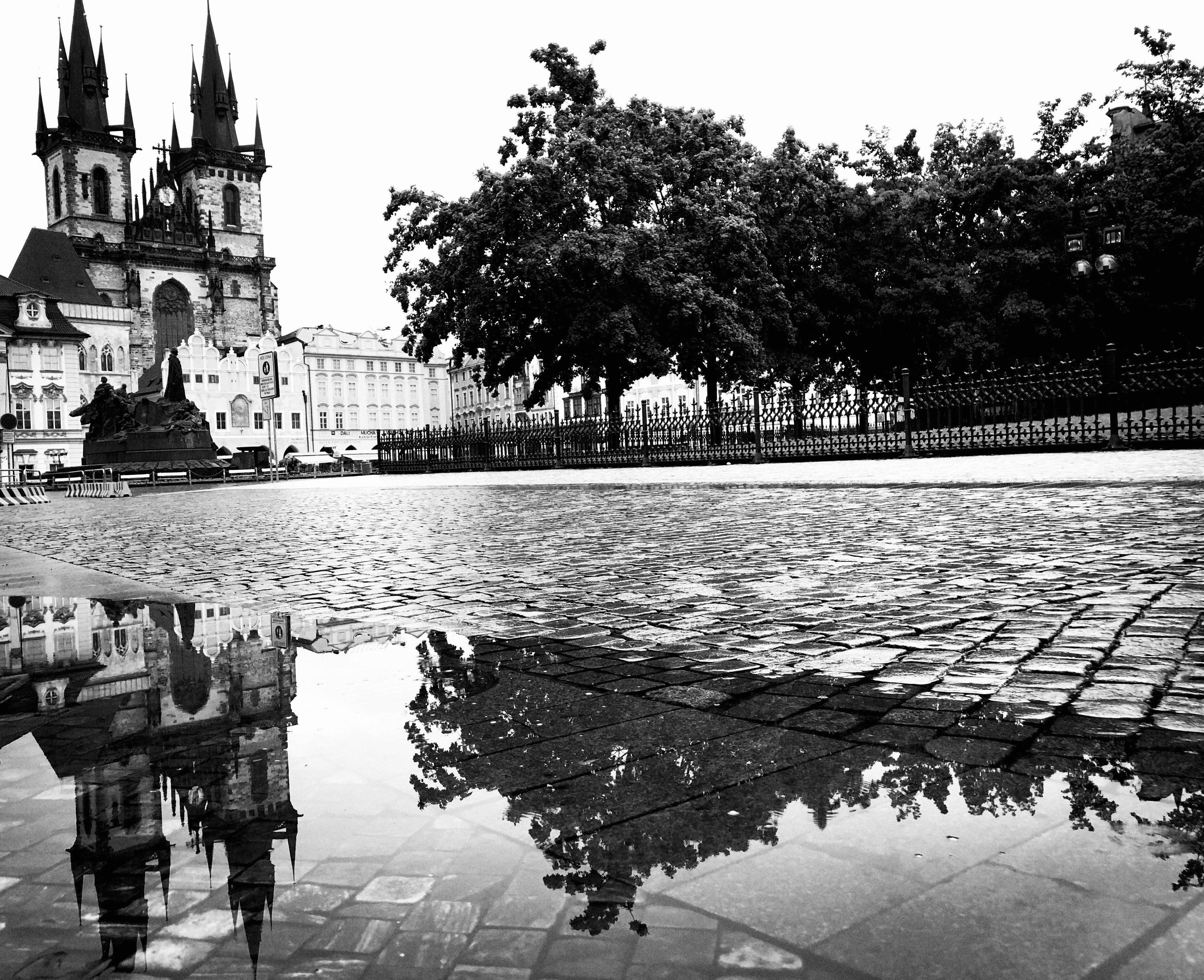 Prague Old Town Square with Gothic church spires reflected in rain puddles on cobblestone pavement