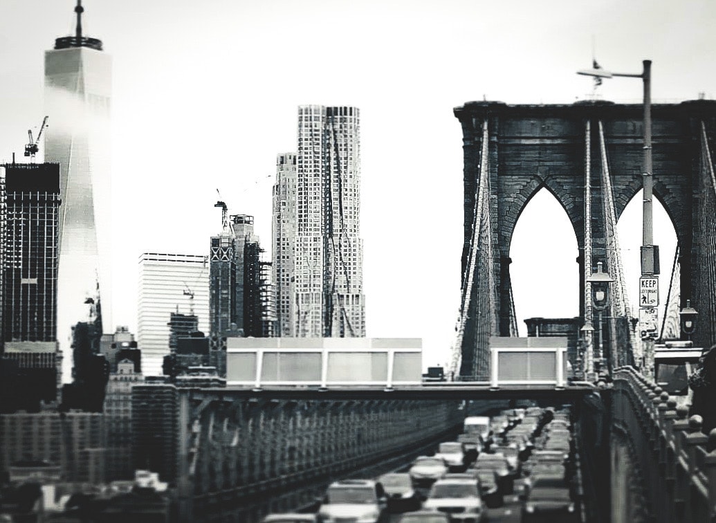 Brooklyn Bridge tower and cables with Manhattan skyline including One World Trade Center in the background, tilt-shift effect