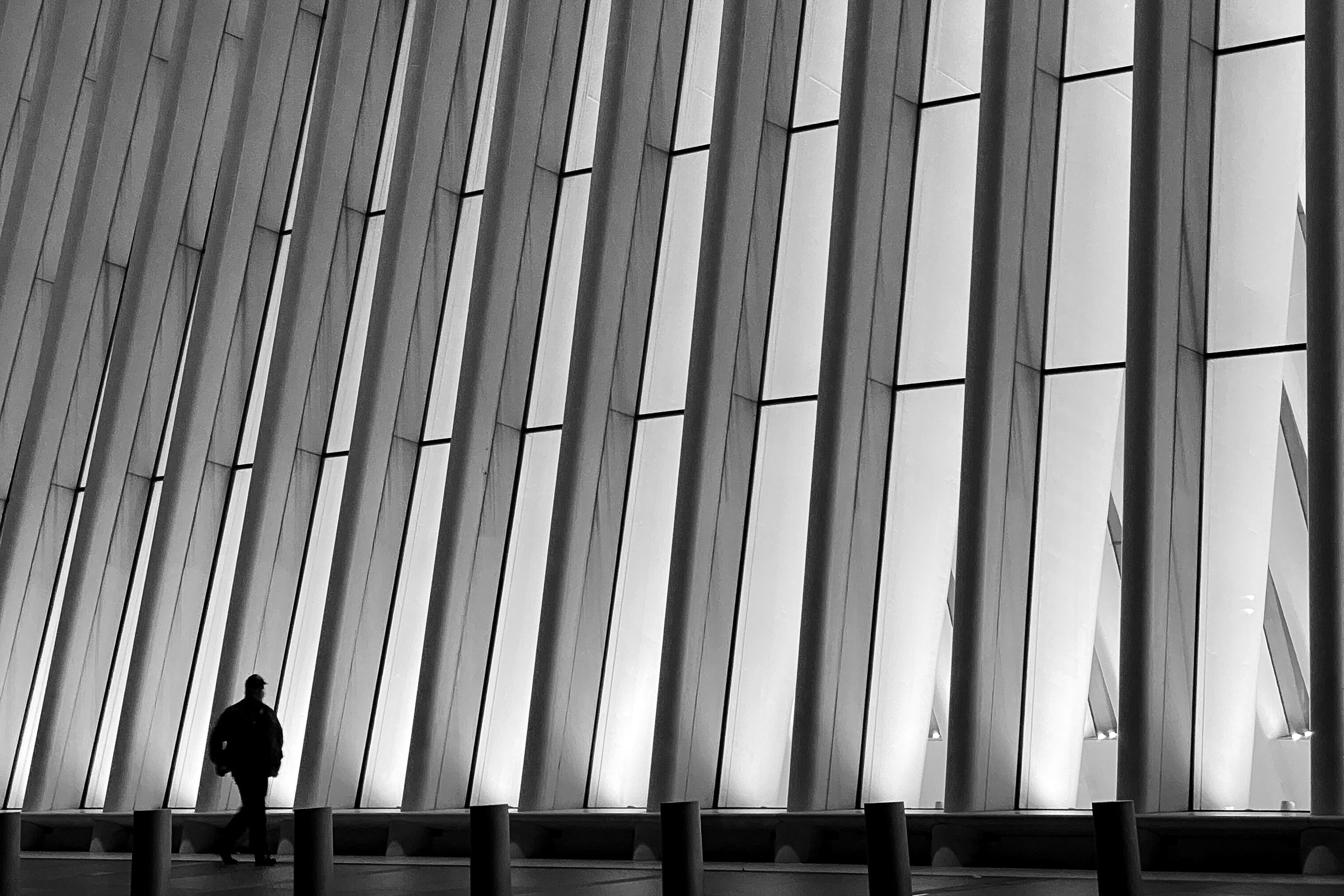Lone silhouetted figure walking beside the towering ribbed white fins of the Oculus transit hub at World Trade Center