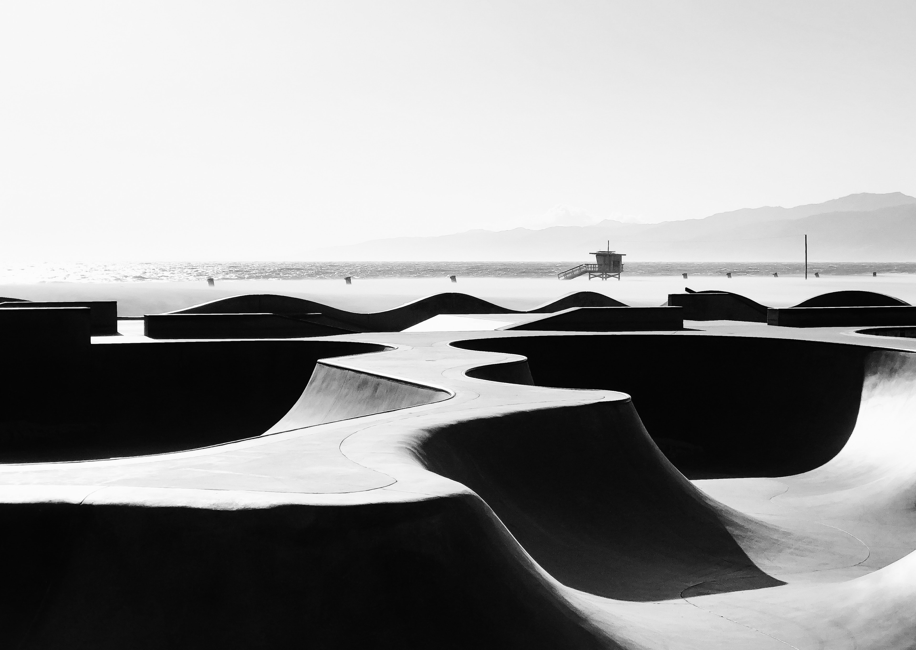 Venice Beach skate park empty concrete bowls and ramps with lifeguard tower and ocean beyond