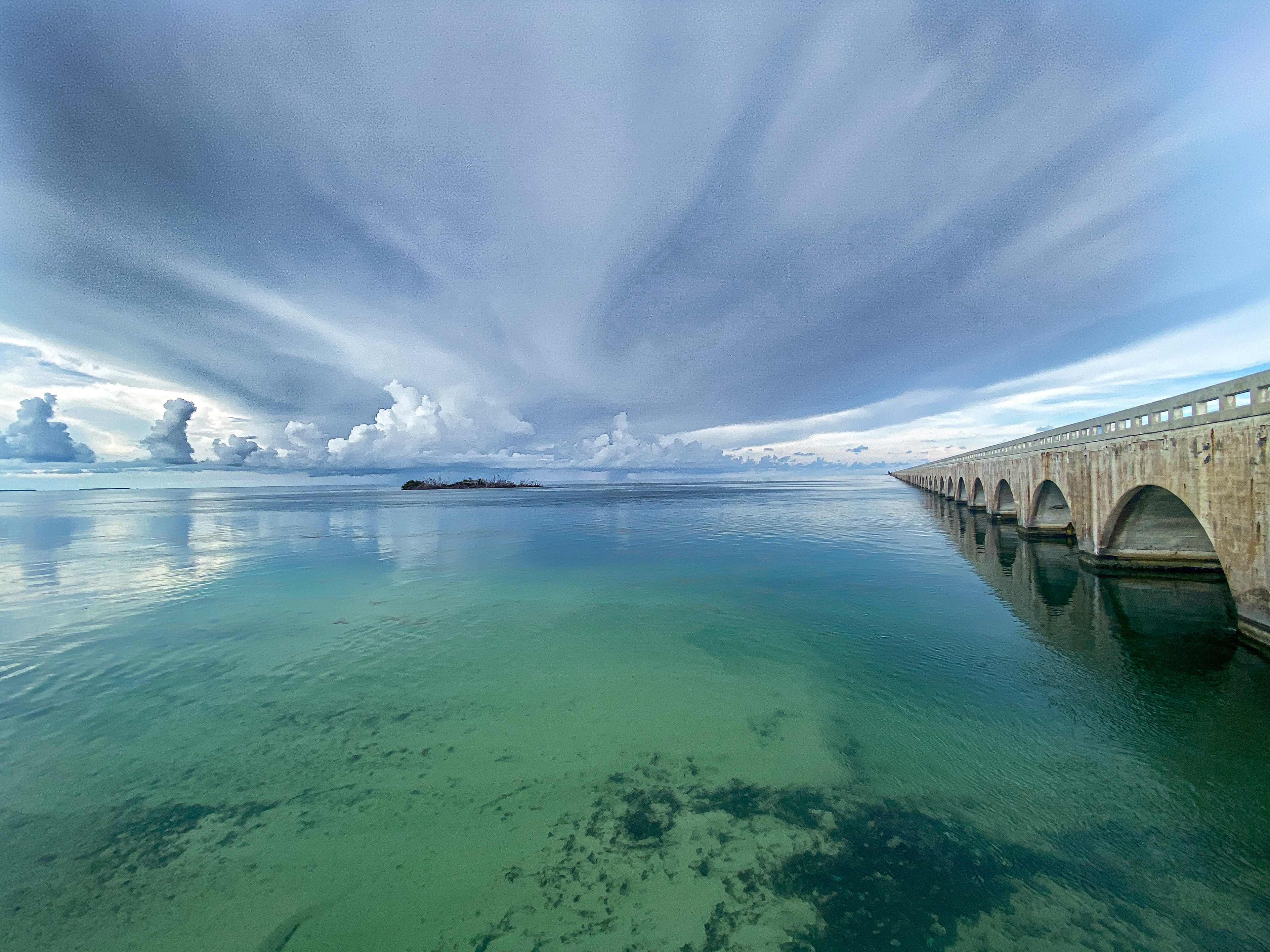 Historic arched bridge spanning turquoise waters under dramatic stormy sky