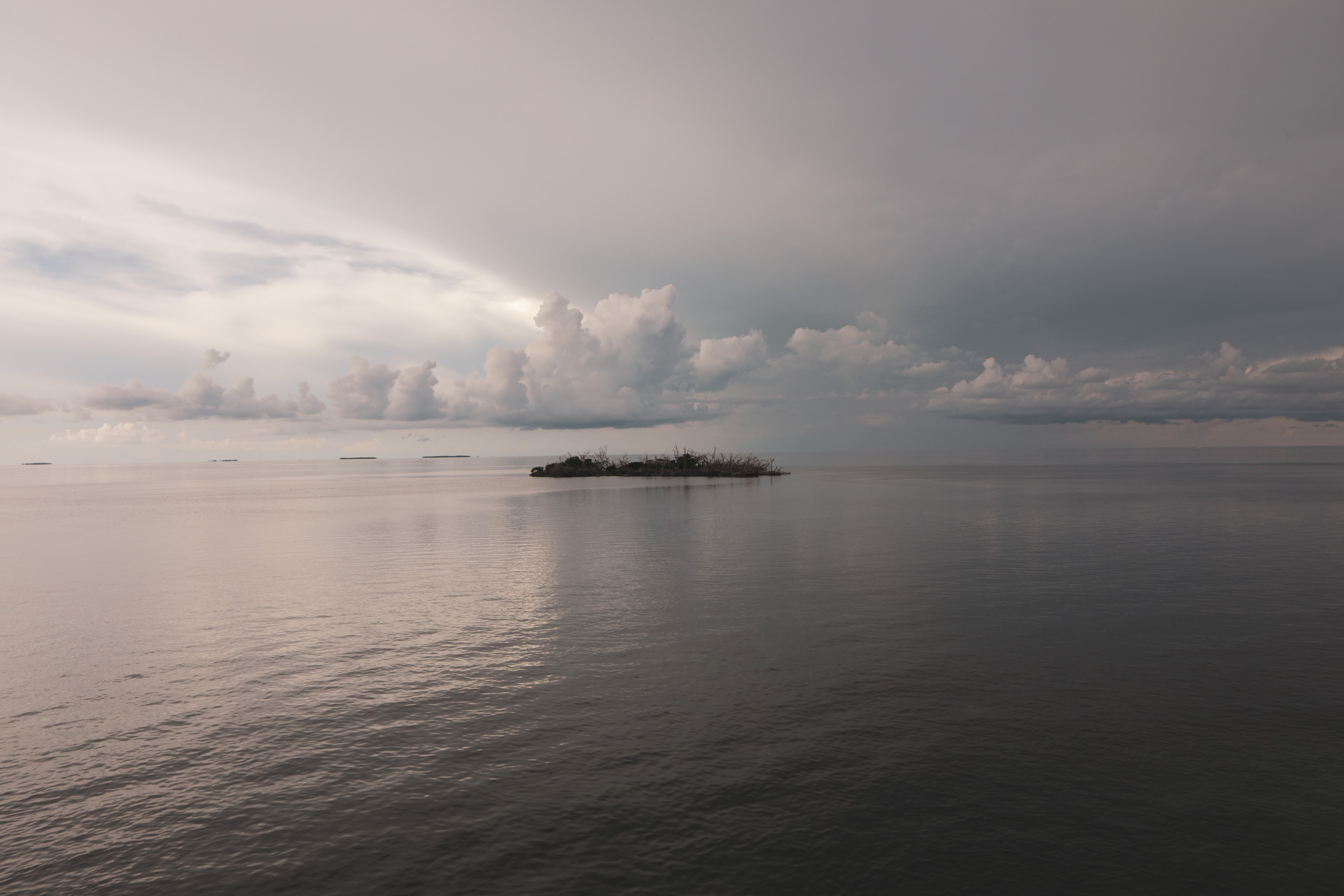 Small island surrounded by calm waters under dramatic clouds
