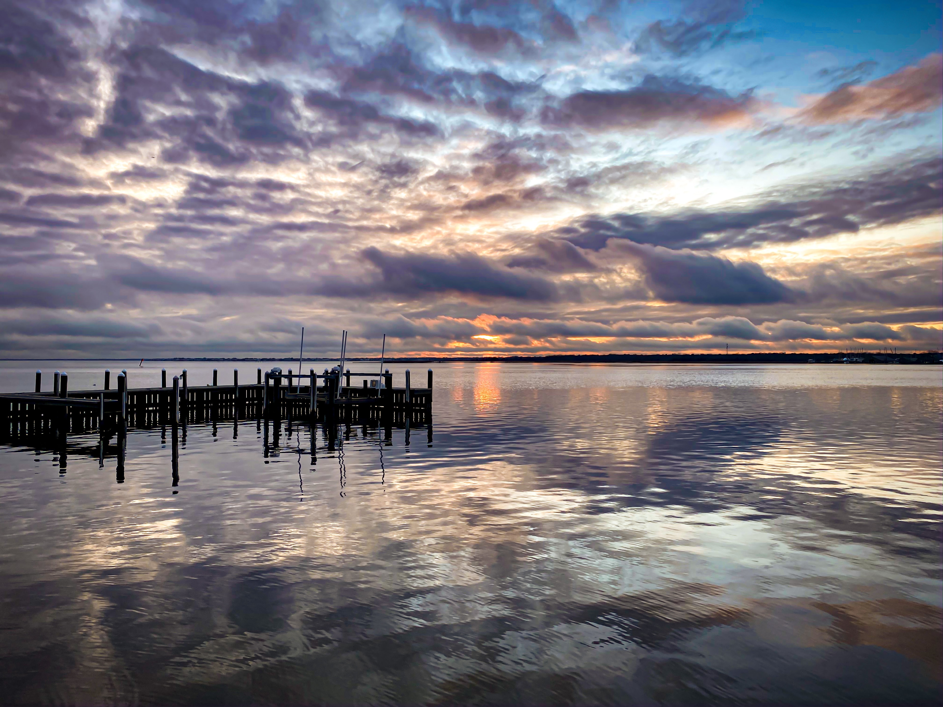 Wooden pier at sunset with dramatic clouds and golden reflections on calm water