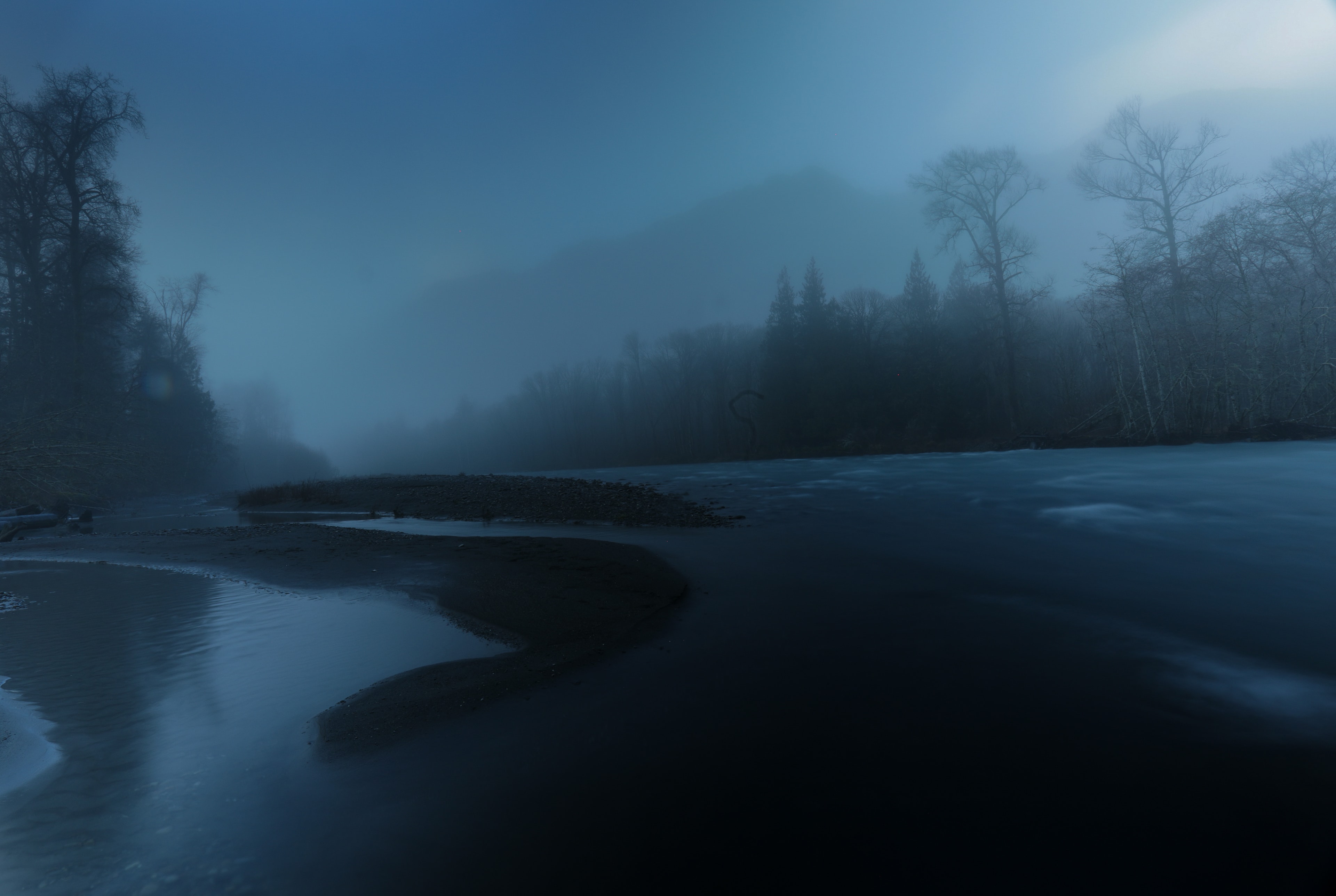 Moody blue night river winding through misty forest with moonlight glow