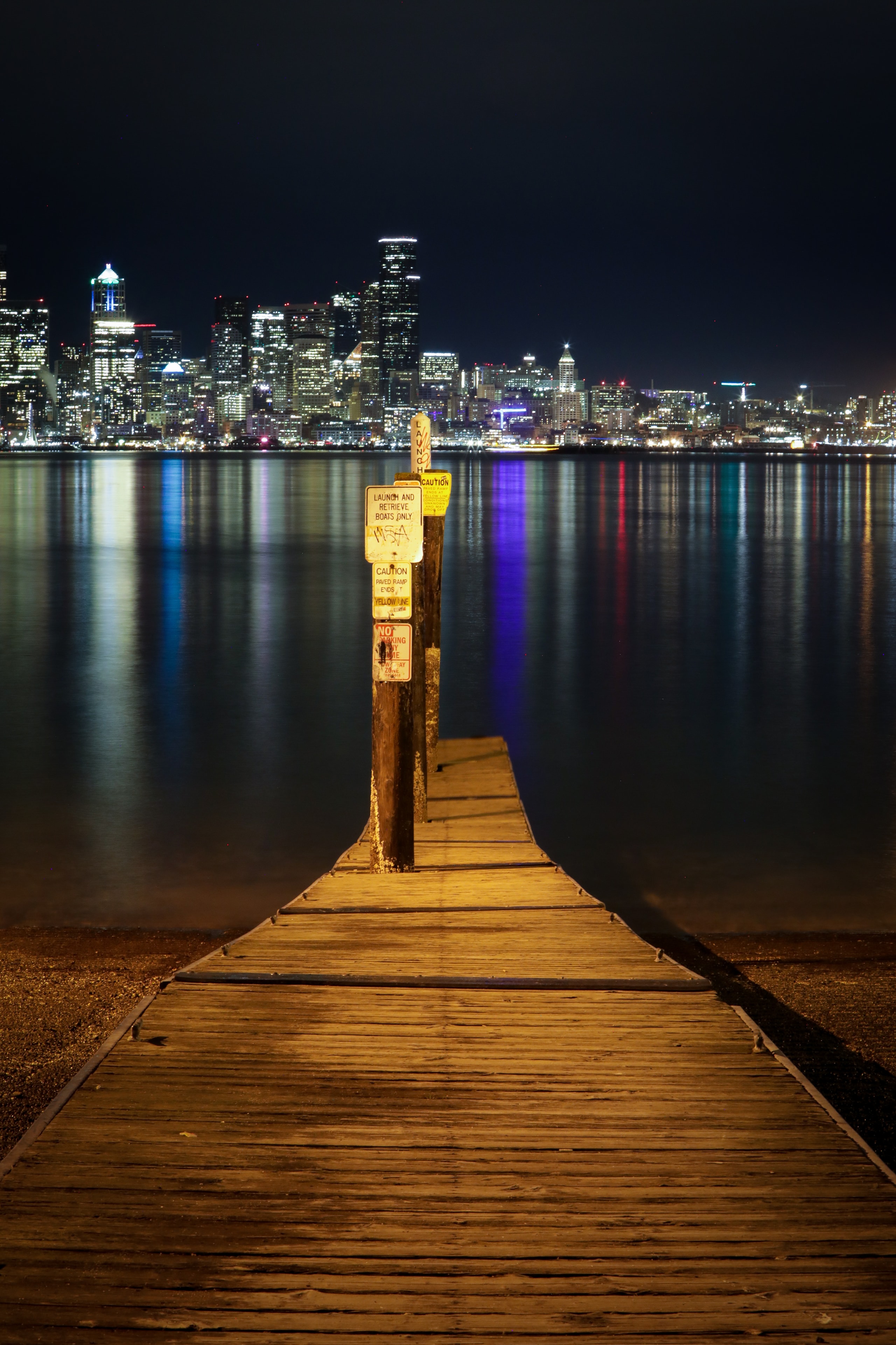 Wooden pier leading toward glittering city skyline reflected in calm water at night