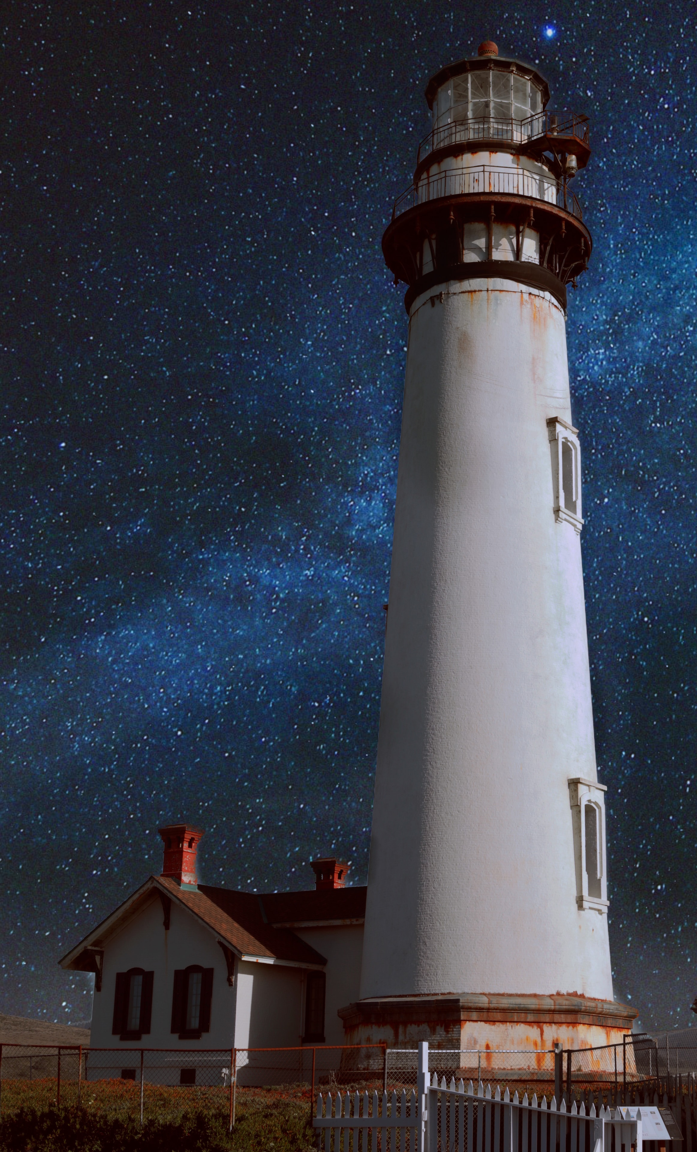 Lighthouse tower rising against a deep blue starry night sky with milky way