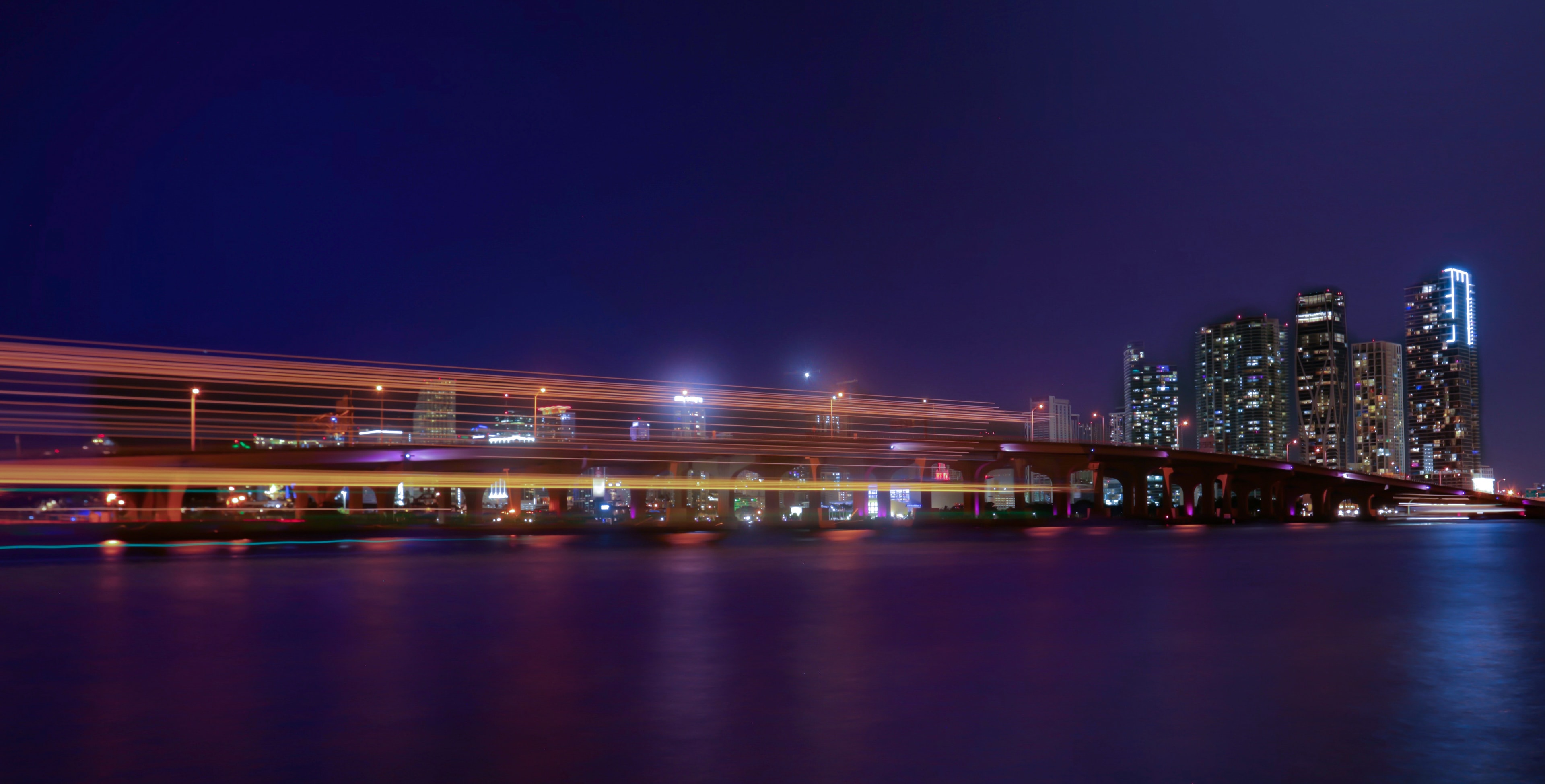 Long-exposure night shot of Miami bridge with golden light trails streaking across the frame over calm bay waters