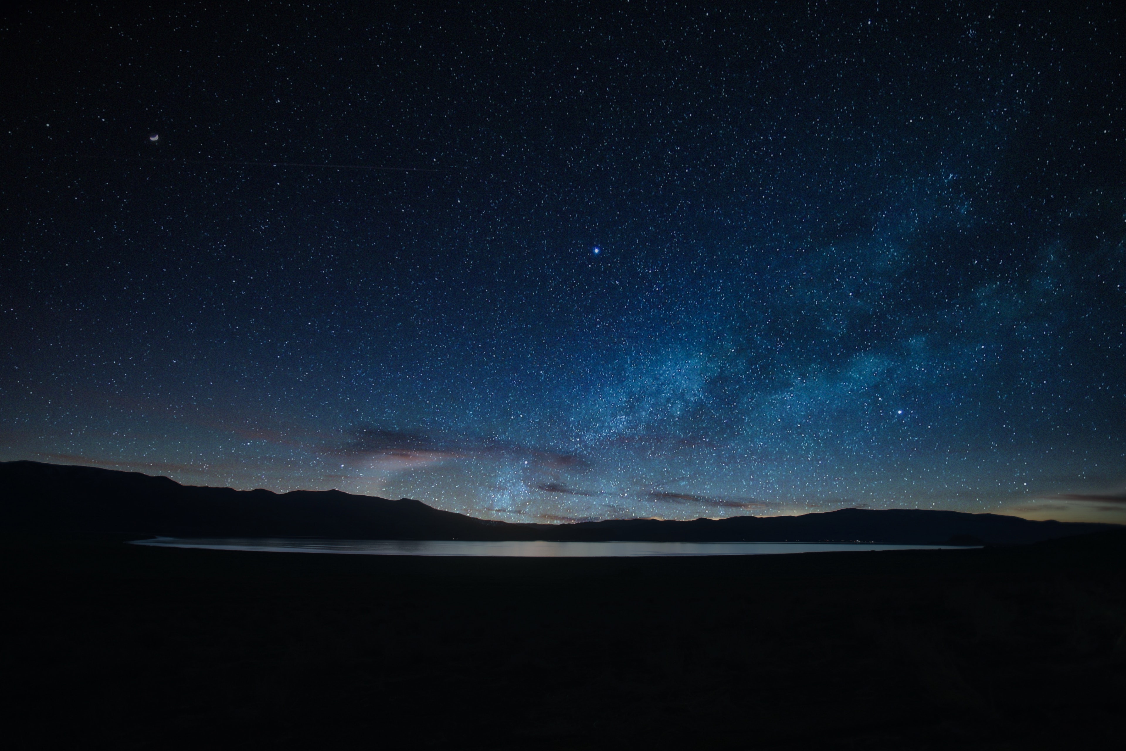 Milky Way galaxy arching over a perfectly still desert lake with silhouetted mountain range under a vast starry night sky