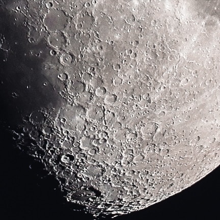 Close-up of the moon's surface revealing intricate crater textures along the terminator line against a black sky