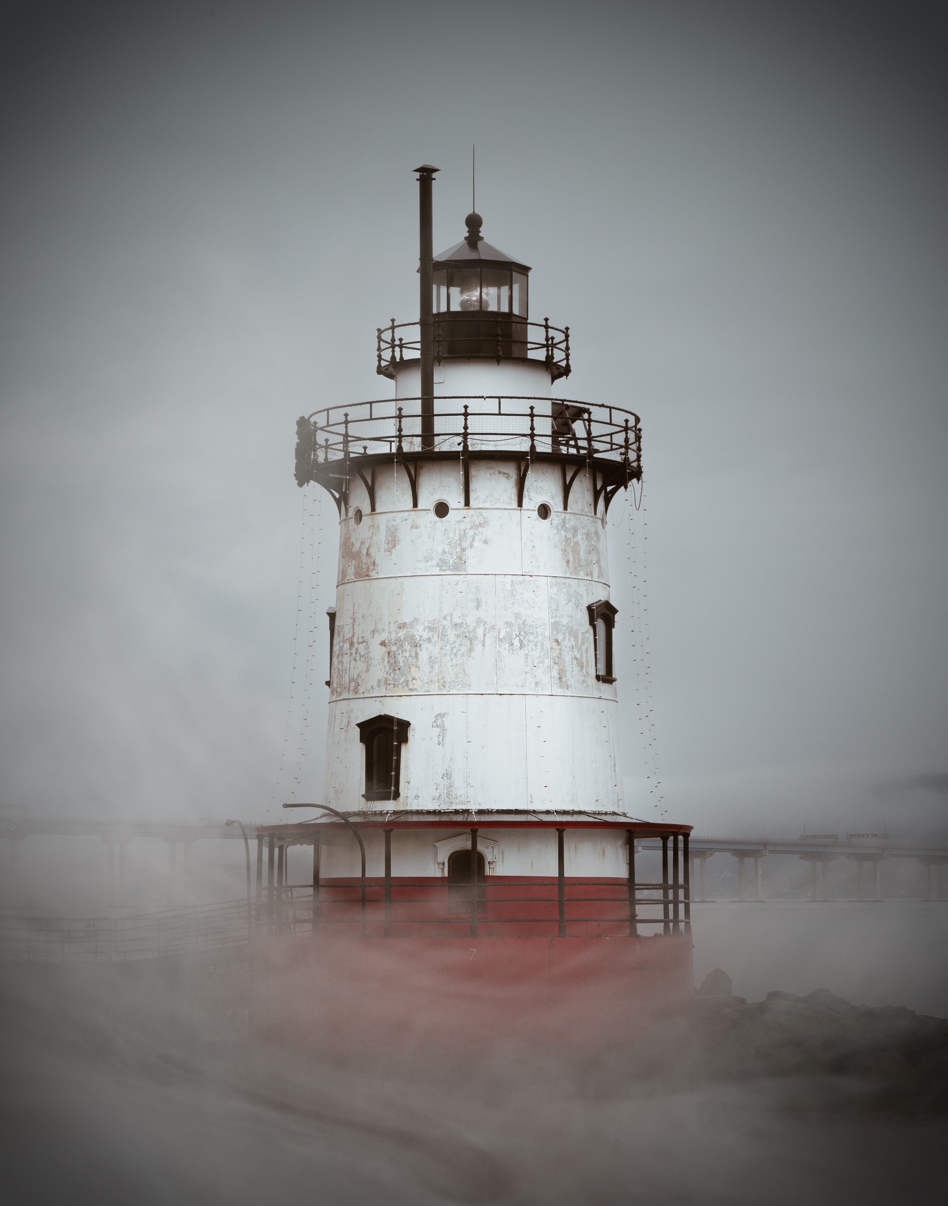 Atmospheric lighthouse with red base emerging from dense fog