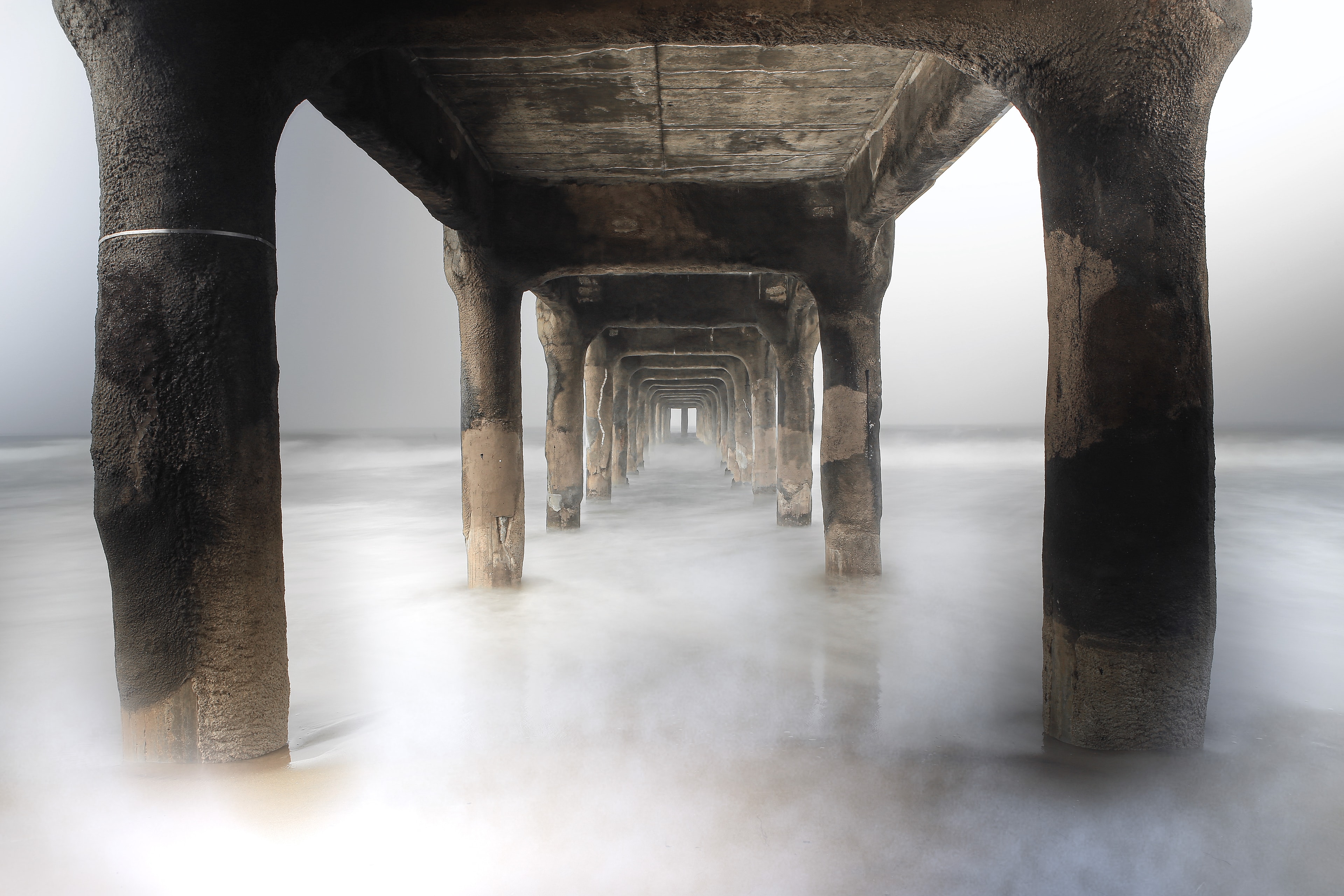 Under a pier looking through receding concrete columns into misty ocean light