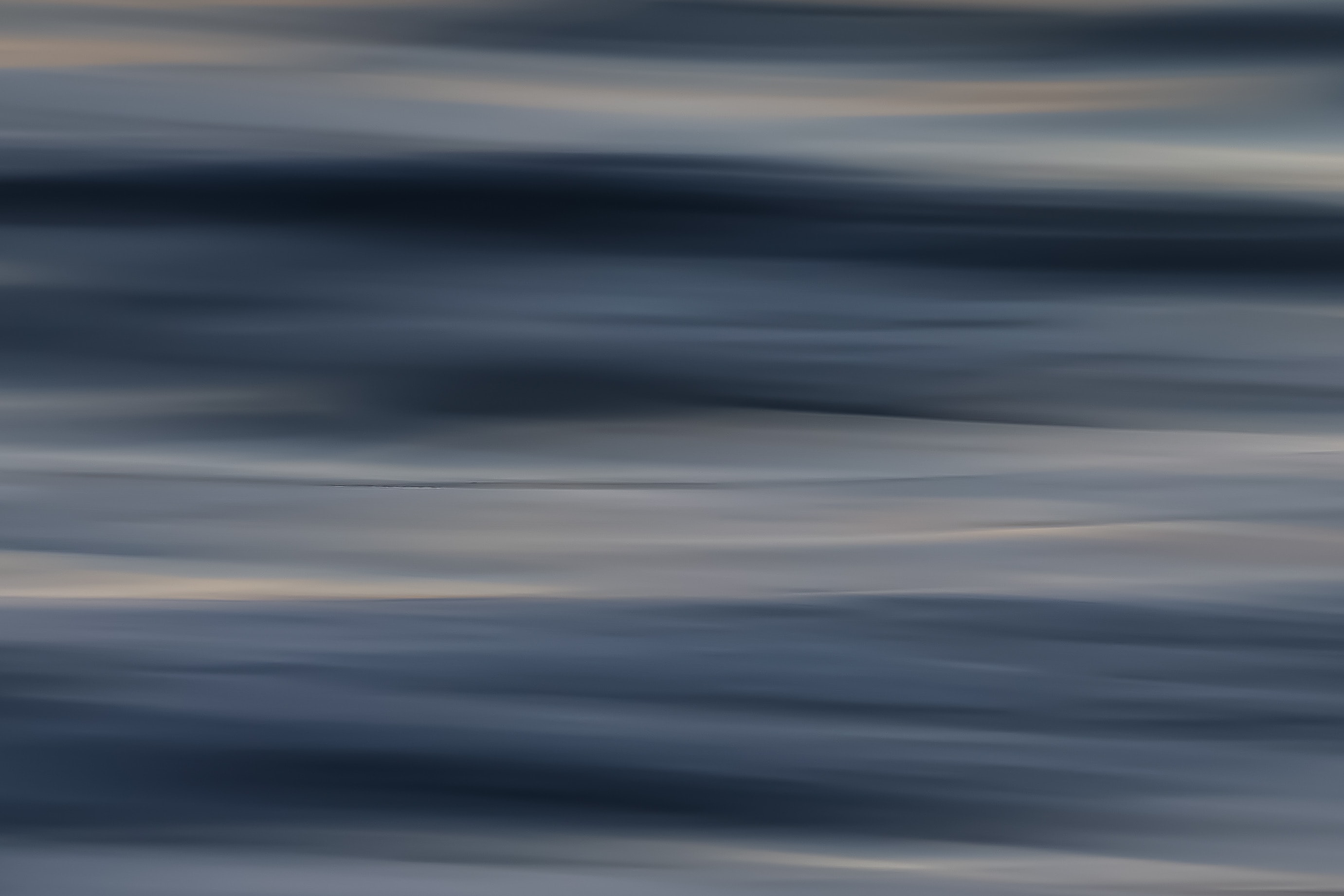 Abstract motion blur seascape with soft blue-grey waves and gentle warm golden glow