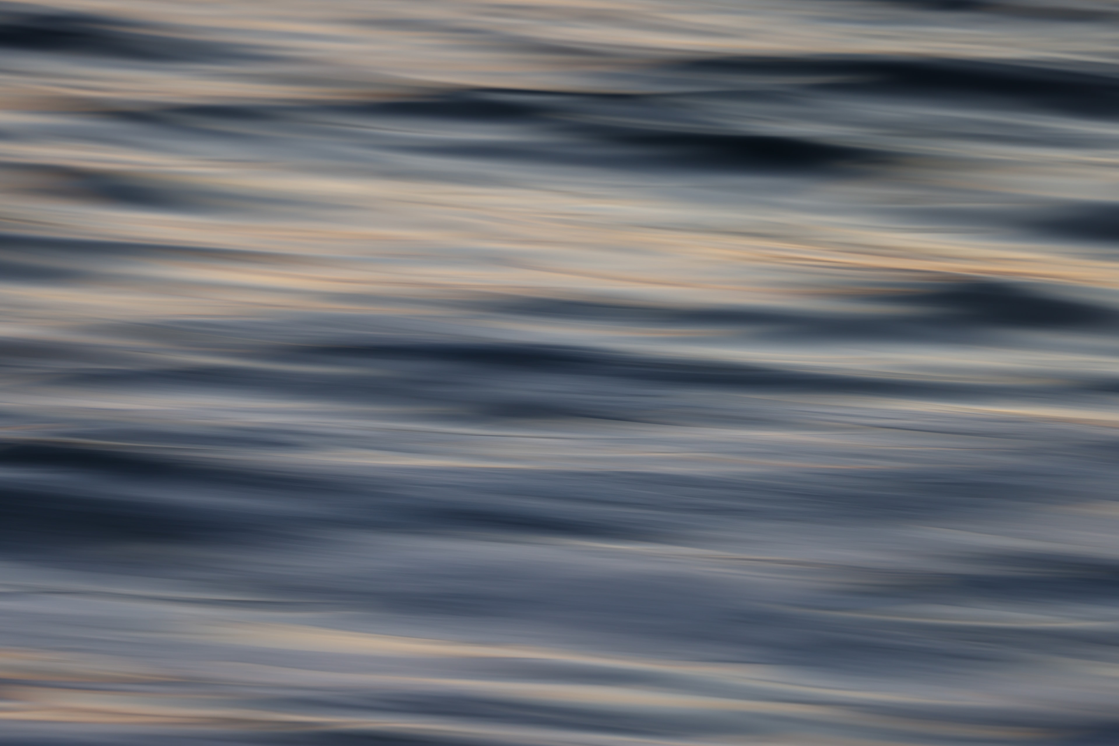Abstract motion blur ocean surface with cool blue-grey waves and soft warm golden highlights