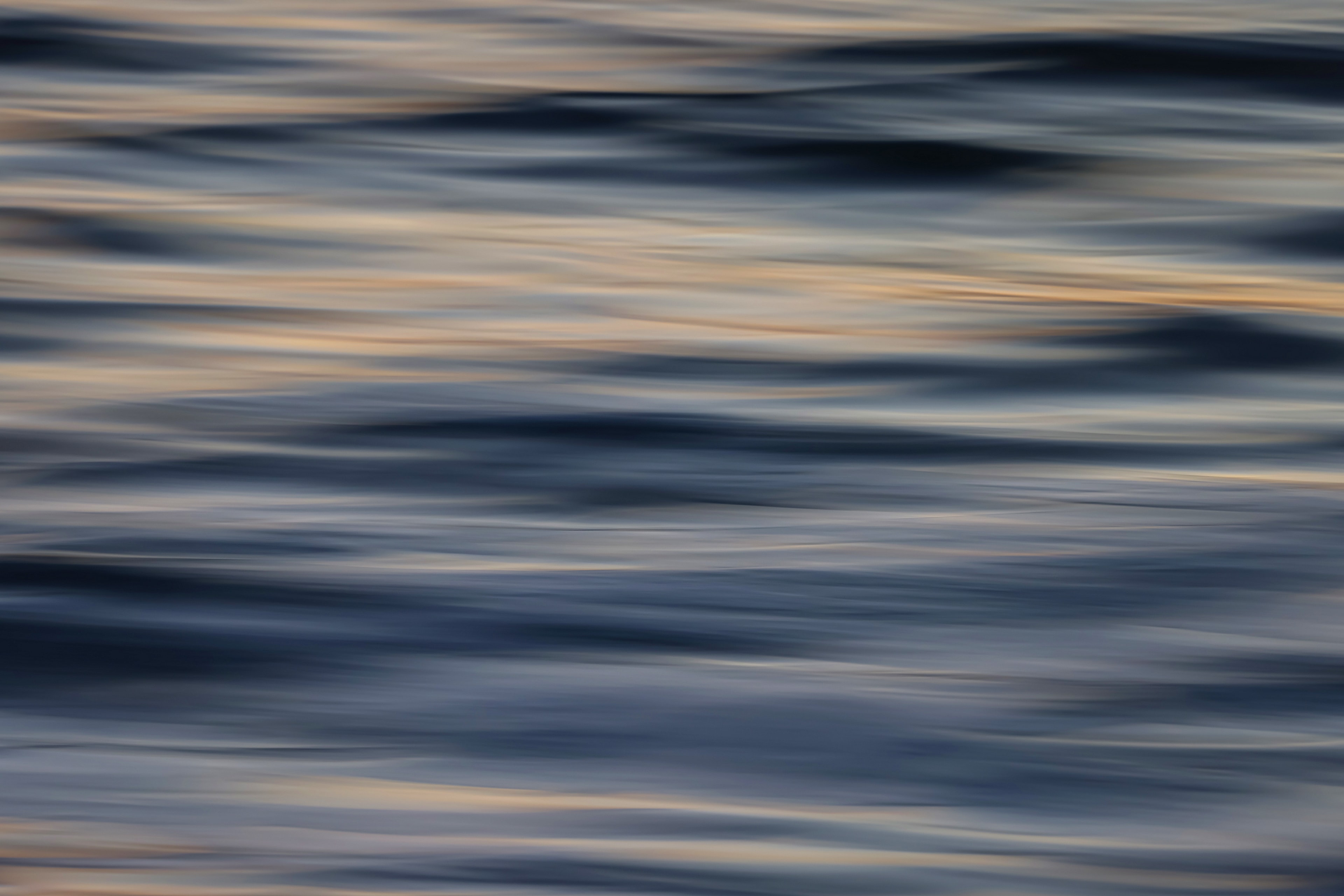 Abstract motion blur seascape with deep blue wave forms and warm peach light reflections