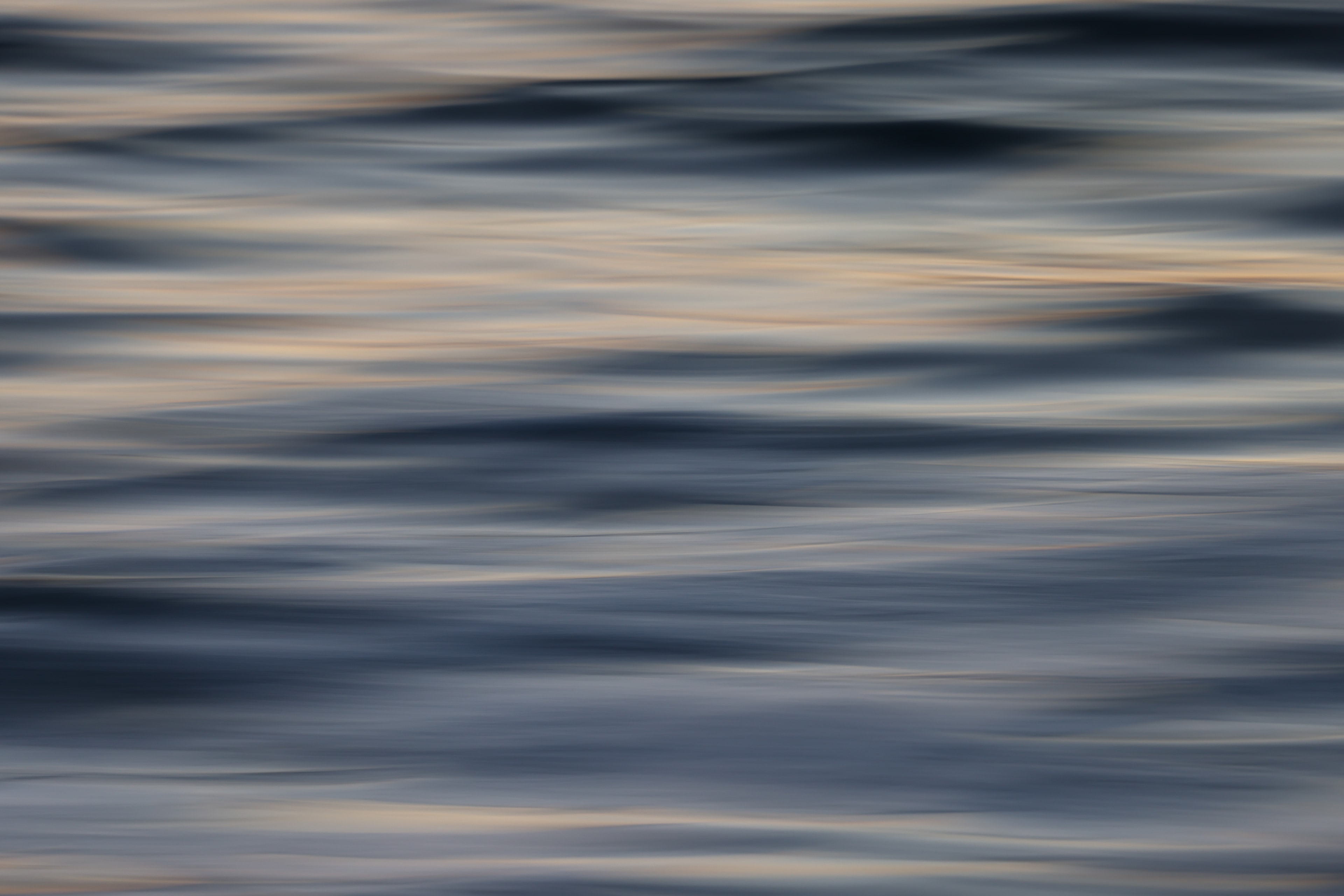 Abstract motion blur seascape with undulating dark blue wave crests and warm golden light bands