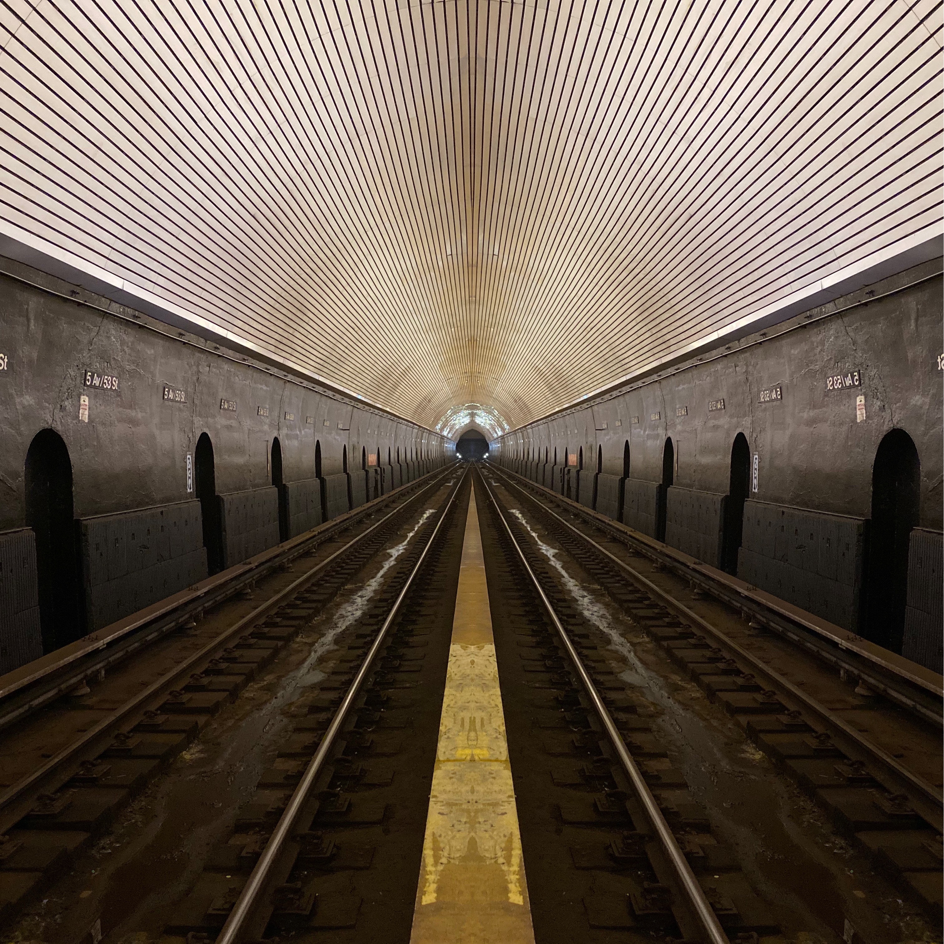 Symmetrical NYC subway tunnel with parallel tracks converging toward distant light