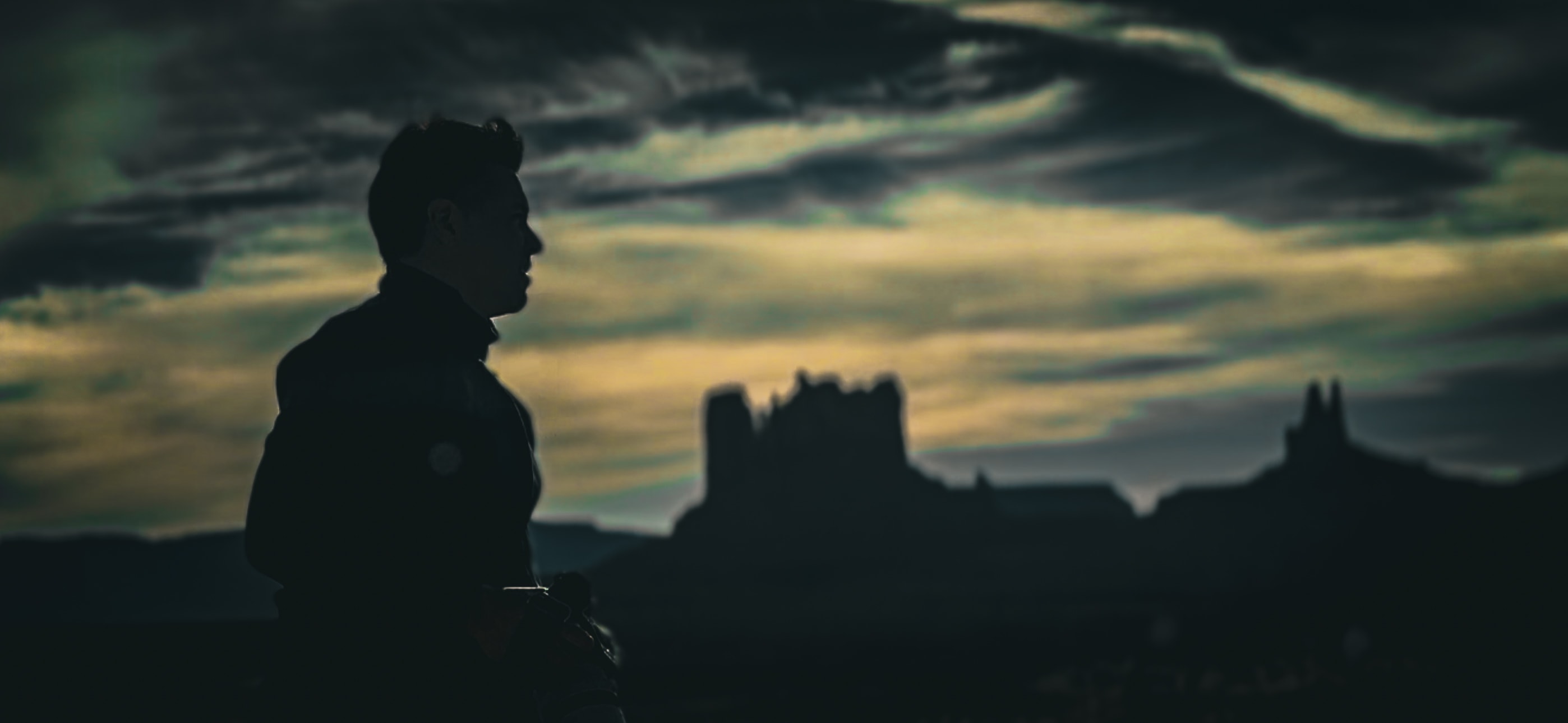 Silhouetted figure with camera overlooking dramatic castle ruins against moody twilight sky