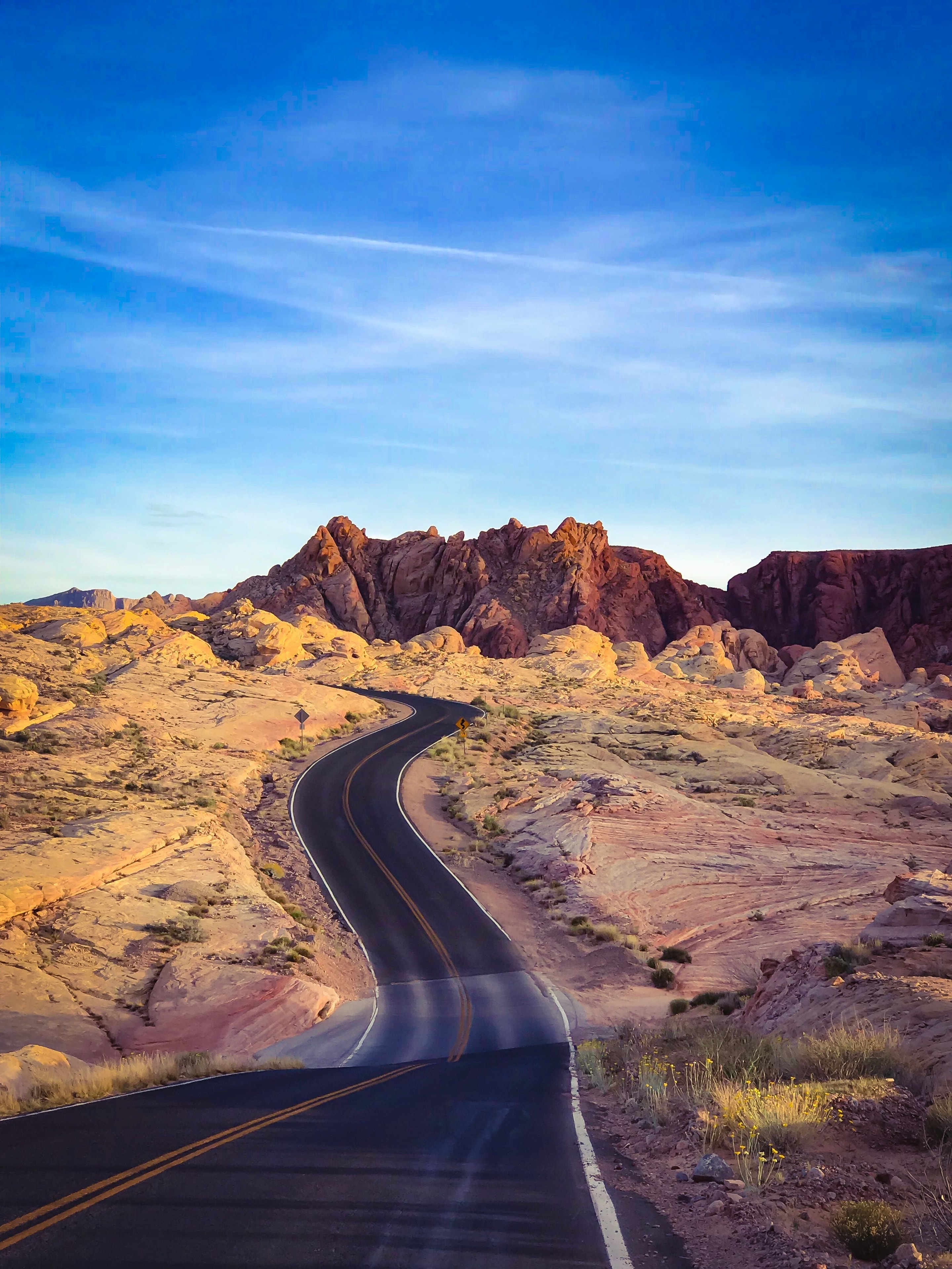 Winding desert road curving through golden red rock formations under vivid blue sky Valley of Fire