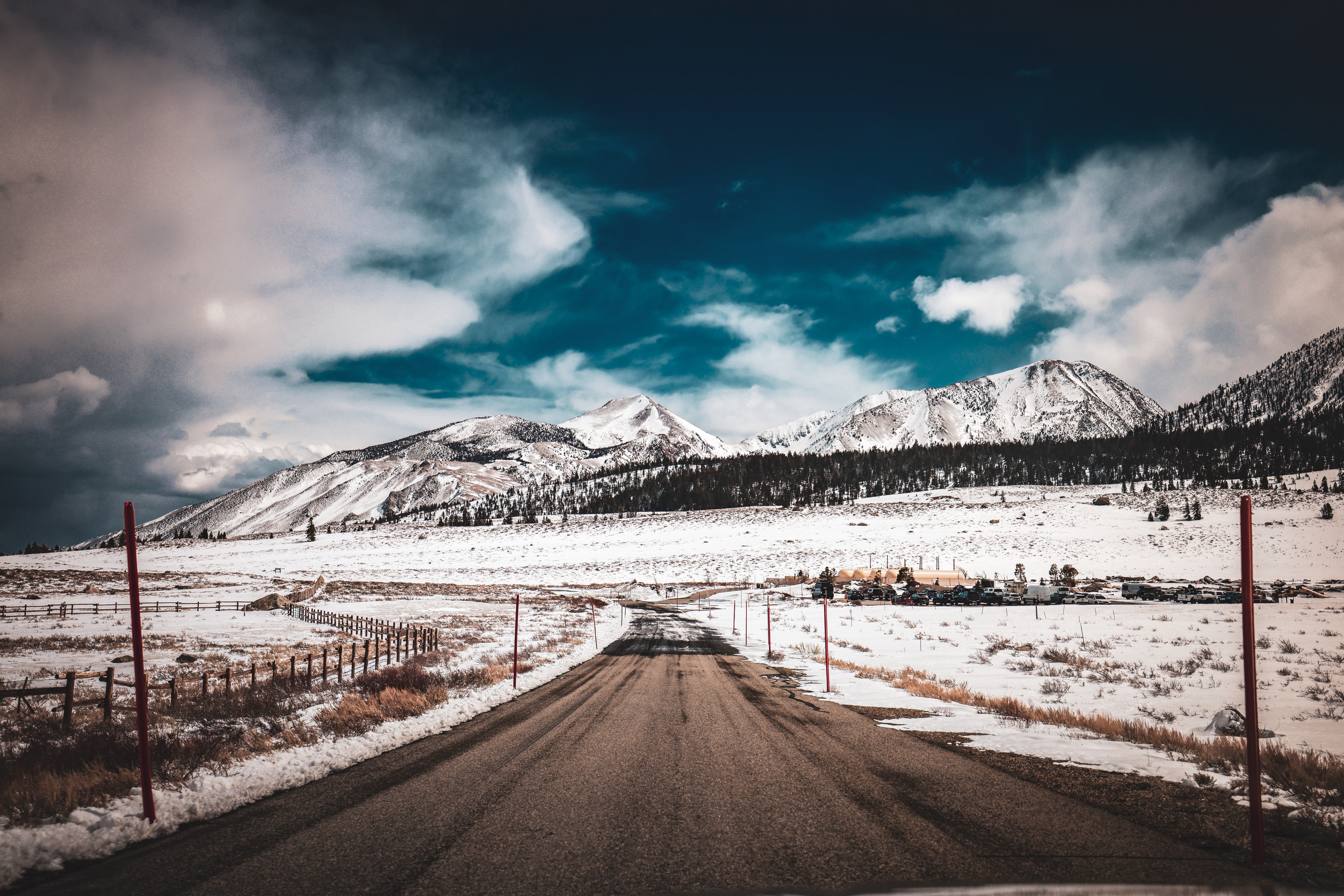 Rural road leading toward snow-capped mountains under stormy blue sky in winter