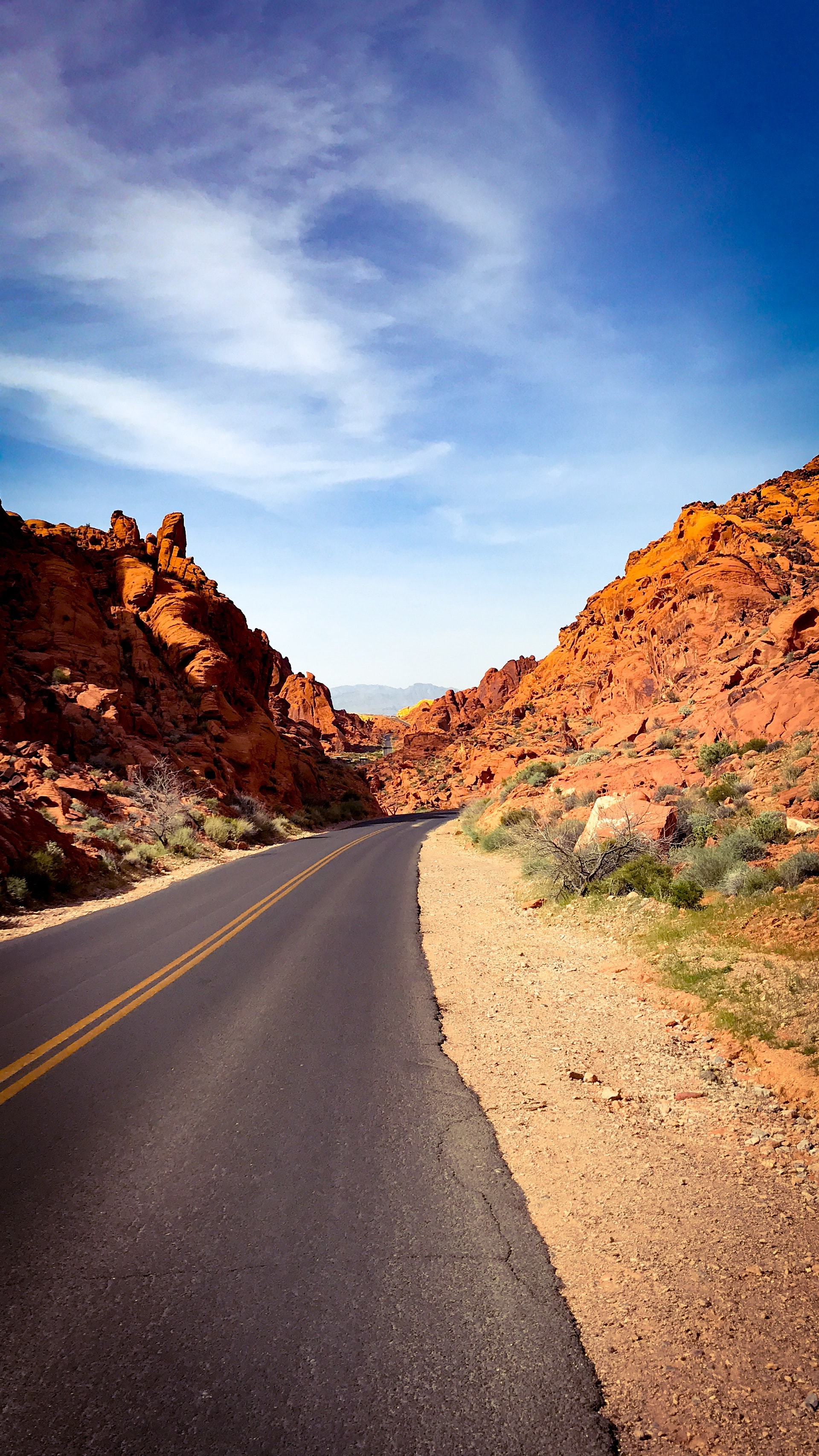 Two-lane road cutting straight through towering red sandstone canyon walls under blue sky