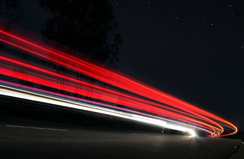 Long-exposure light trails of vehicles curving through the night under a starry sky