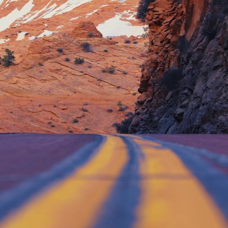 Low angle of winding road through red rock canyon with yellow center lines