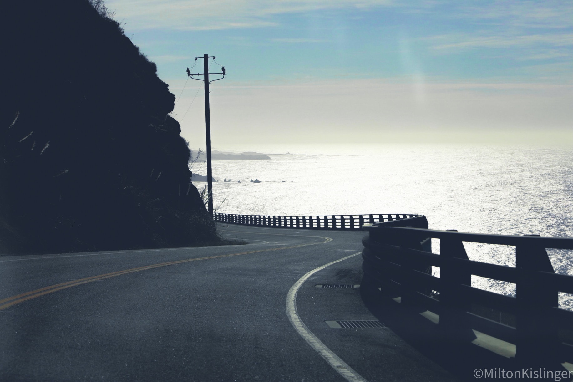 Coastal highway curving along rocky cliffs above shimmering silver ocean