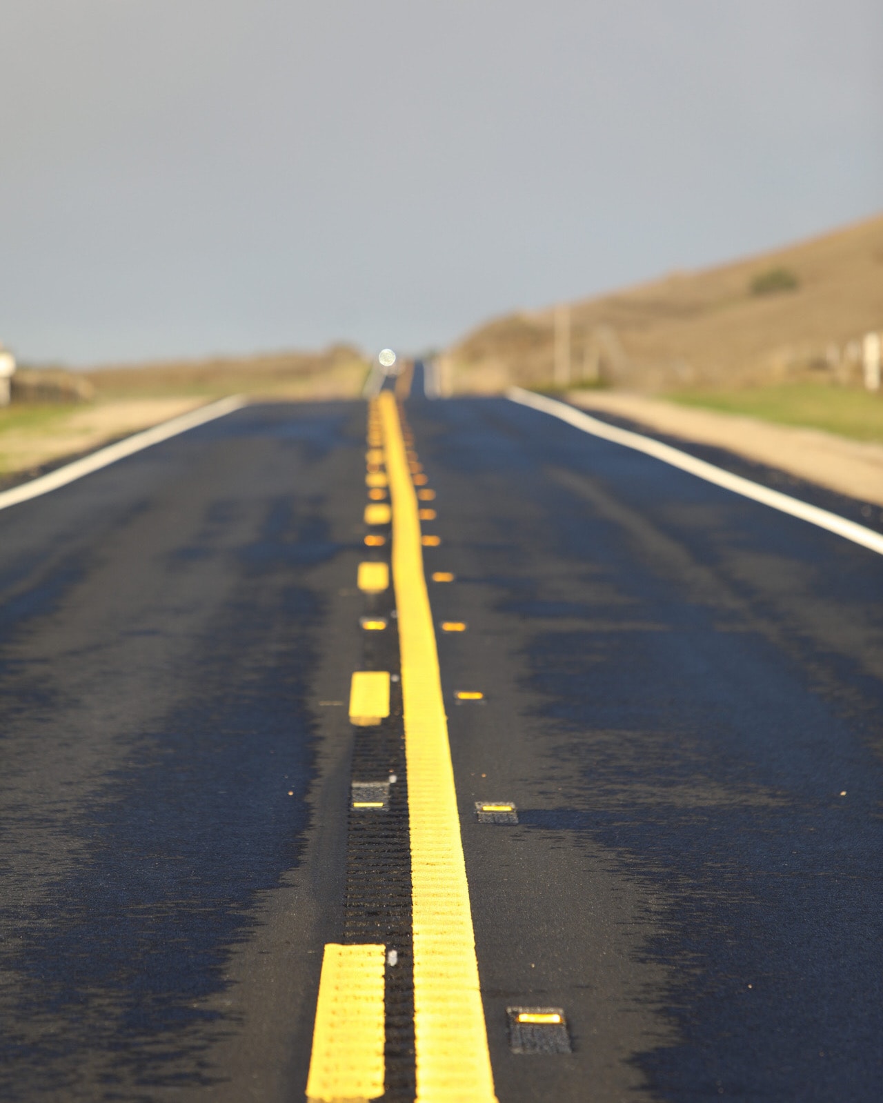 Empty straight road with bold yellow center line stretching to the horizon under pale sky