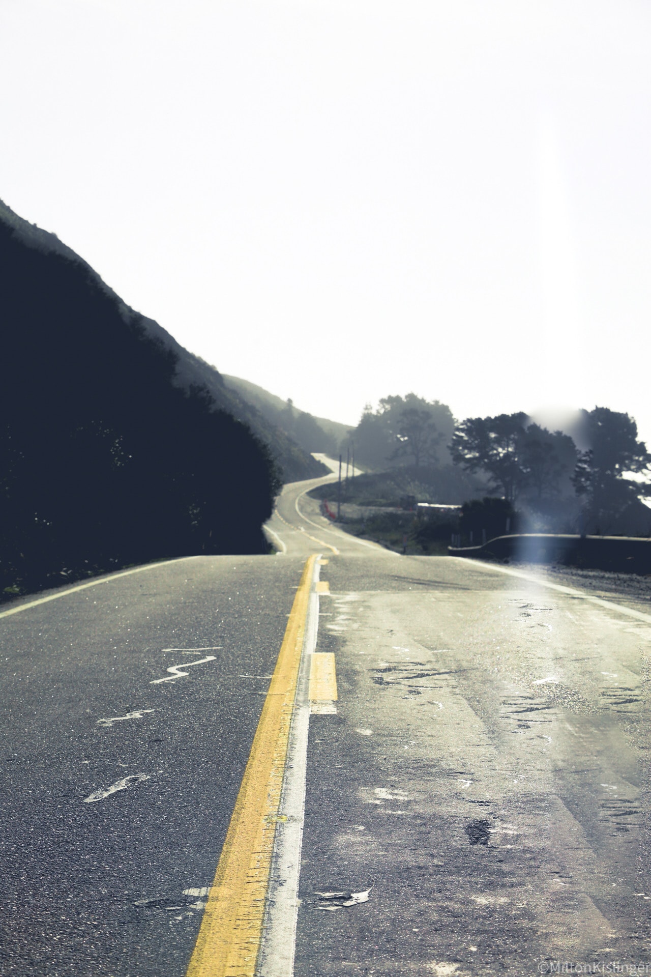 Winding coastal road climbing through misty hills with soft backlit haze