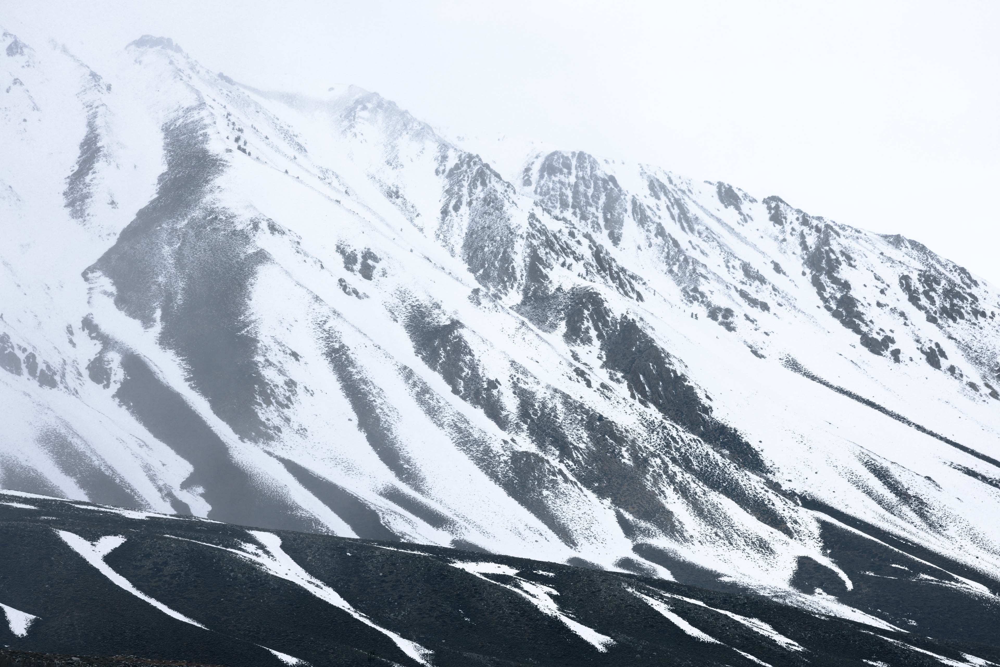 Snow-covered mountain ridgeline with dramatic diagonal shadows and misty white sky
