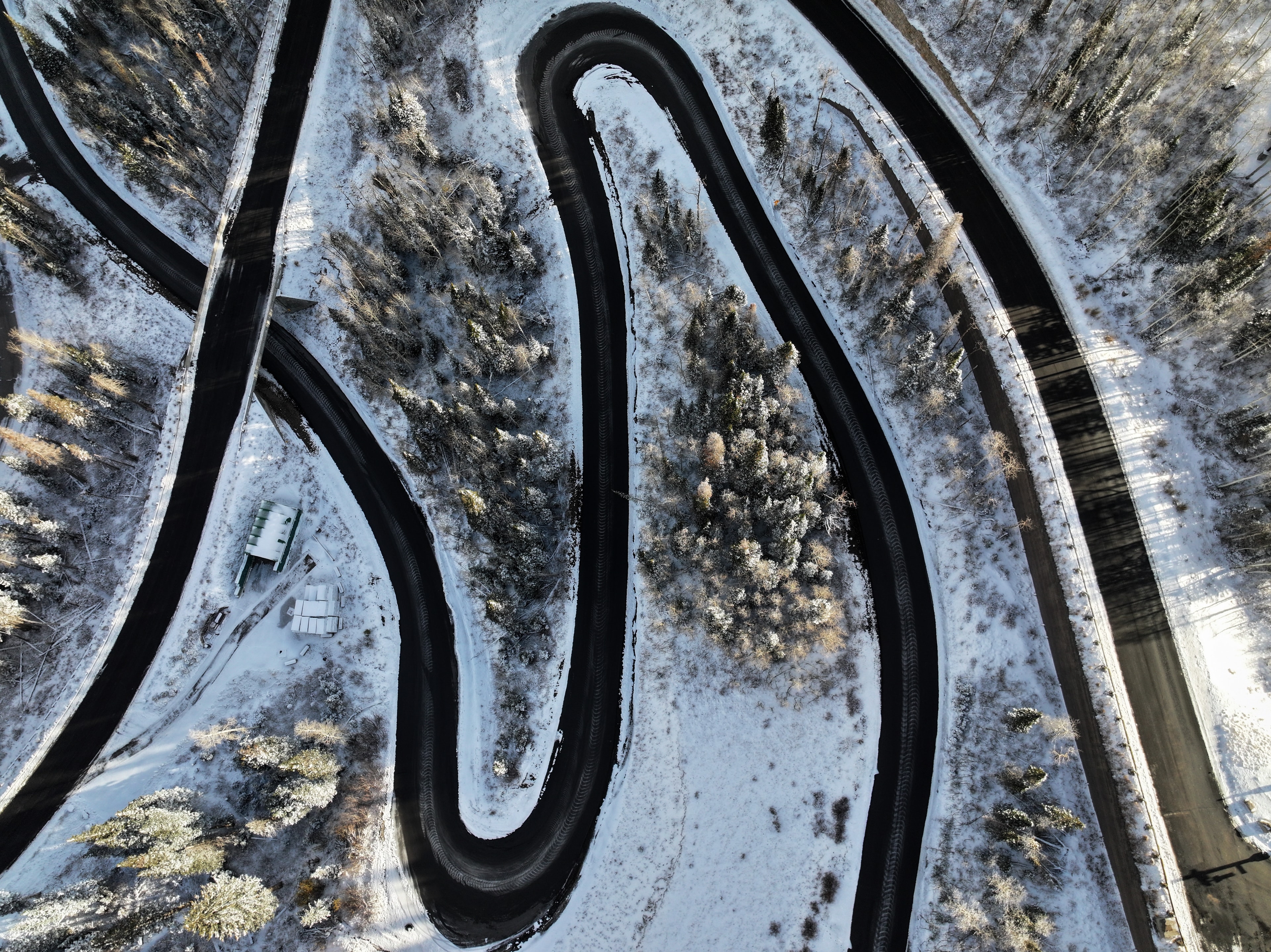 Aerial top-down view of serpentine switchback roads weaving through snow-covered terrain with frost-dusted evergreens between the curves