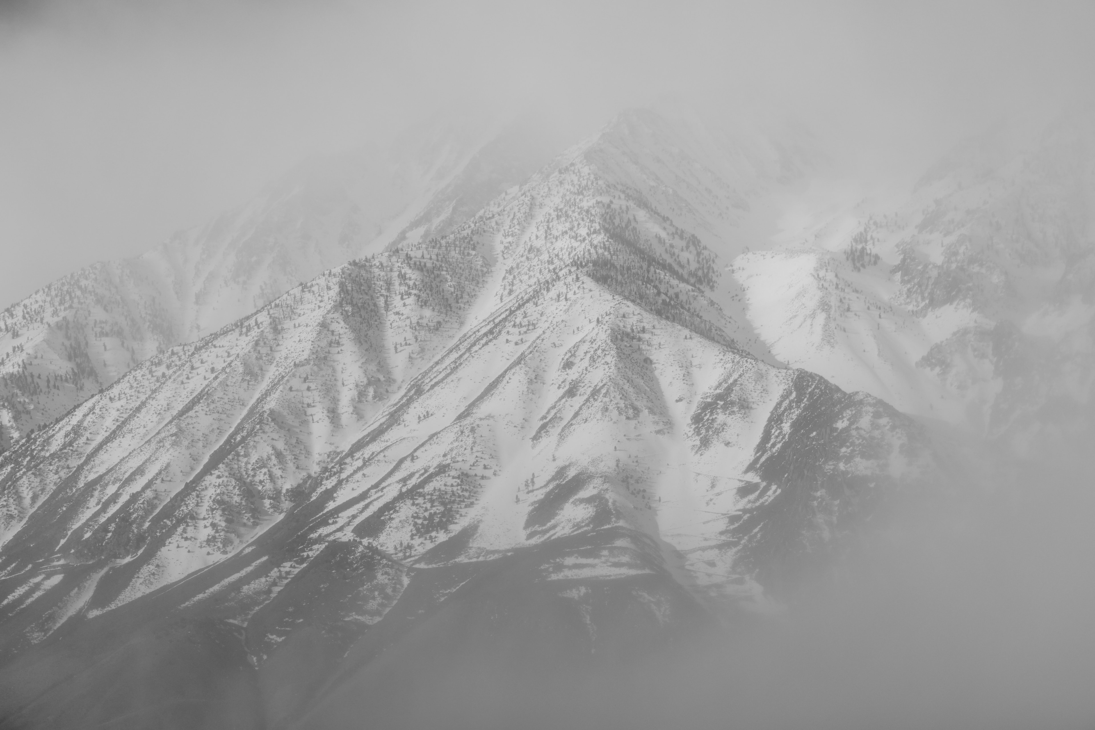 Snow-capped mountain peak emerging from thick fog and mist in monochromatic tones