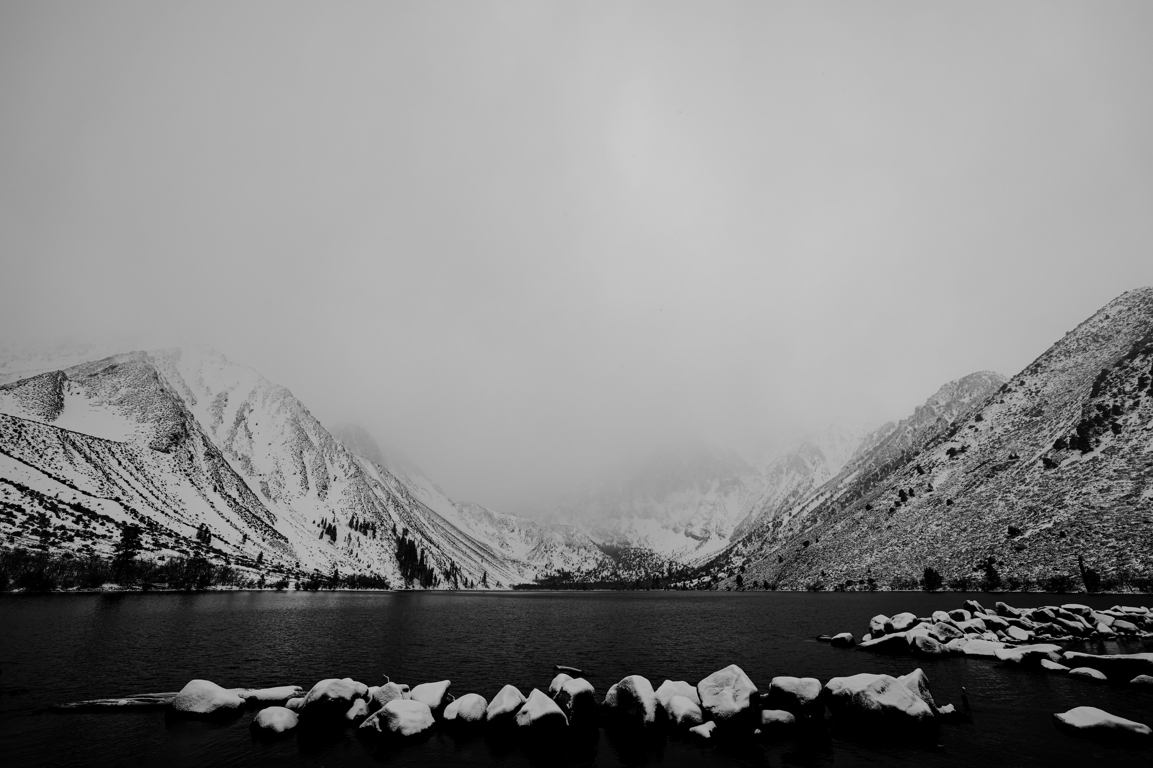 Black and white frozen alpine lake flanked by snow-covered mountains under overcast sky