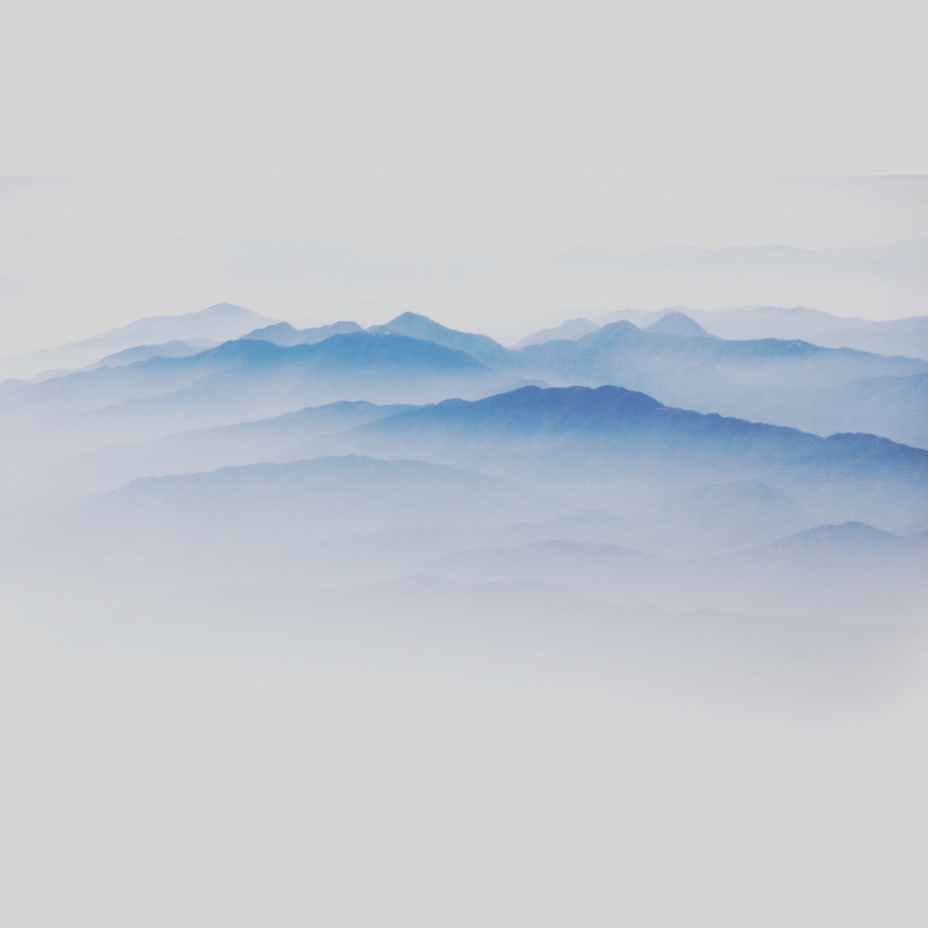 Layered blue mountain ridges receding into soft white mist aerial view